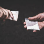 A drug deal taking place. One hand holding cash, and the other holding drugs.